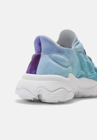 Zapatilla deportiva con un upper de textil en un degradado de azul claro a violeta, cuello acolchado y una gruesa suela de goma blanca con agarre texturizado.