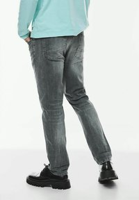 Grå denimjeans med en avslappnad passform, försedda med bakfickor och subtila slitningar, kombinerade med svarta snörskor.