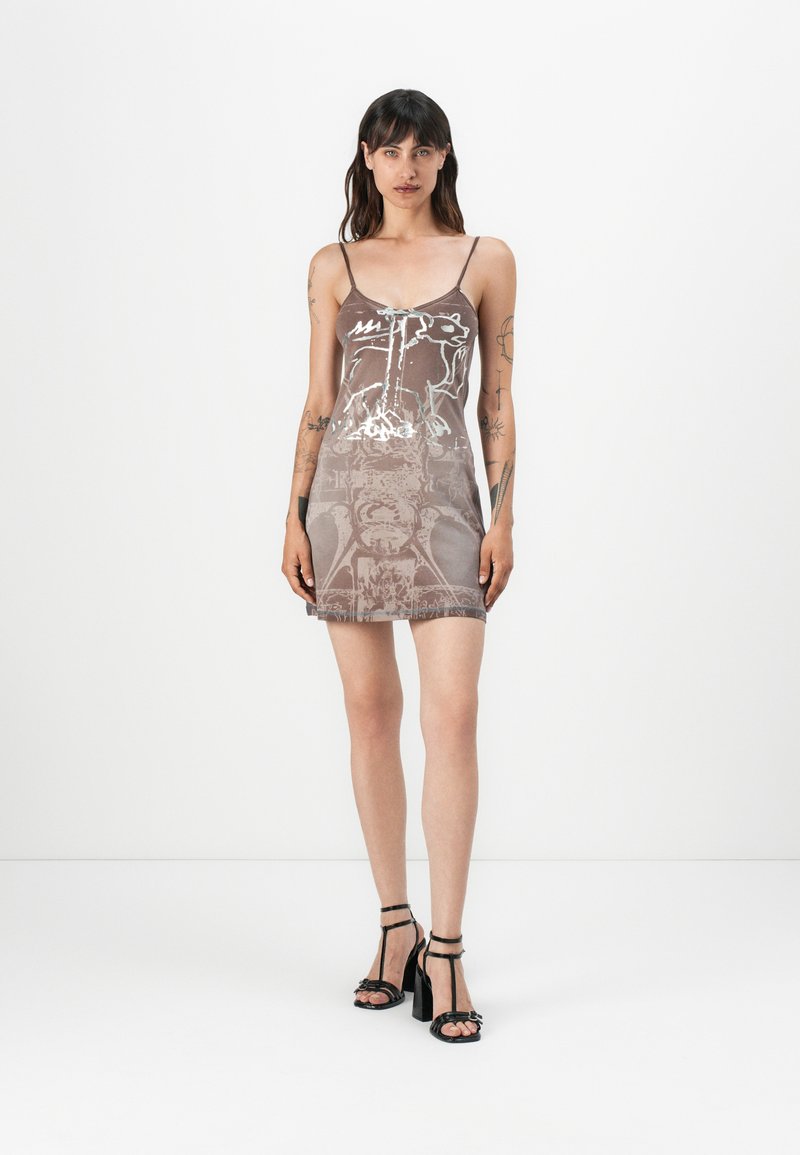 Satin mini dress in brown with white graphic print, featuring thin straps and a fitted silhouette, paired with black strappy high heels.