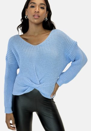 Suéter de punto azul claro con escote en V y diseño de frontale retorcido, combinado con leggings negros y brillantes. Presenta mangas largas de corte holgado.