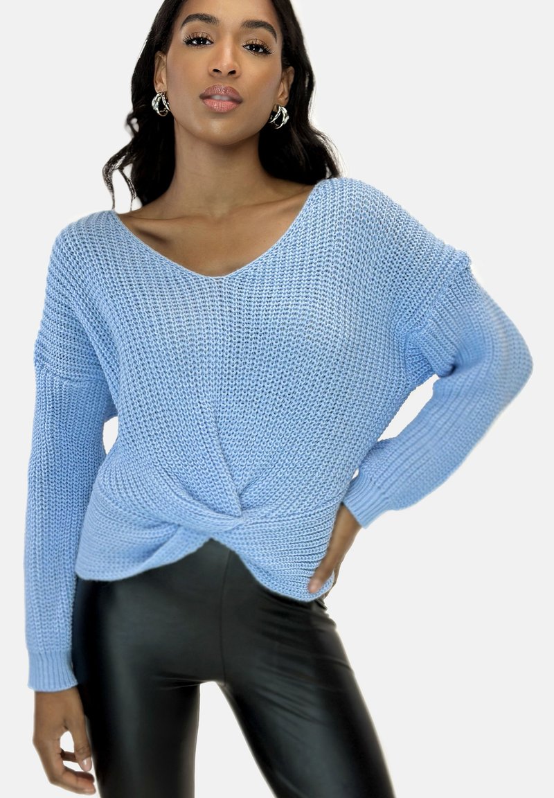 Hellblauer, gestrickter Pullover mit V-Ausschnitt und gedrehtem Frontdesign, kombiniert mit schwarzen, glänzenden Leggings. Besitzt lockere, langärmlige Ärmel.
