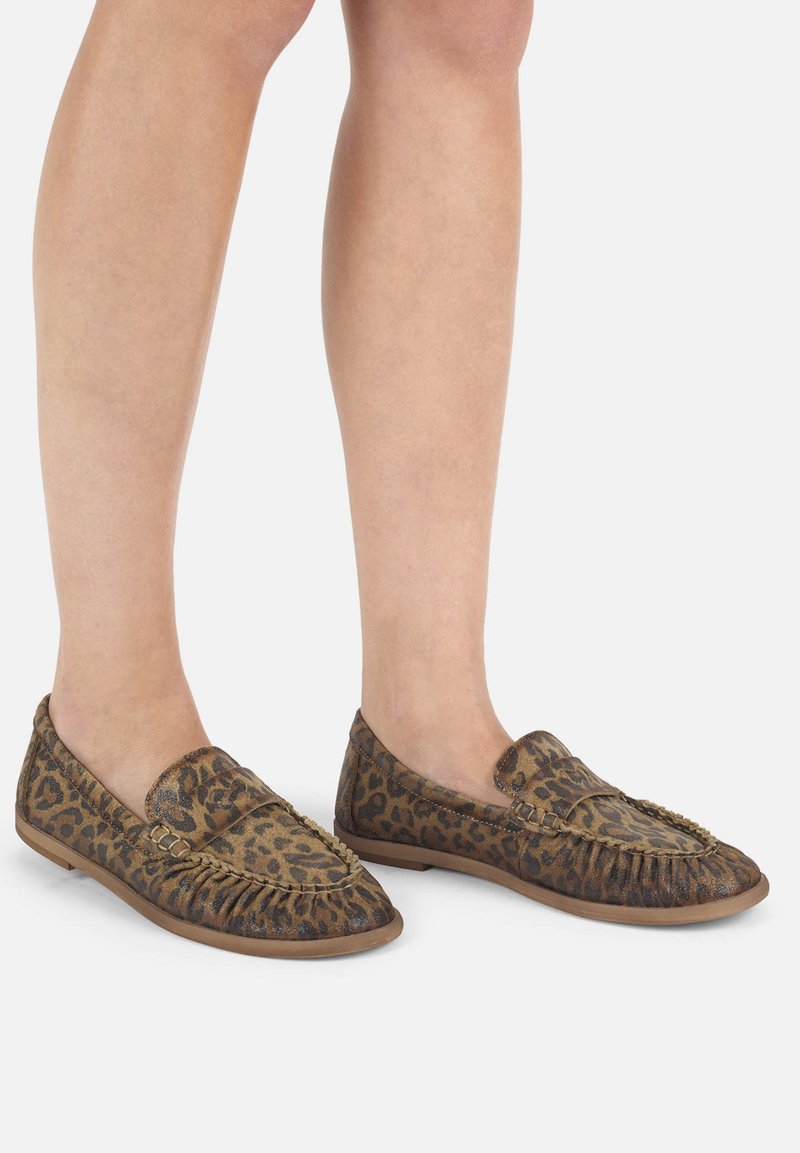 Lederpuschen mit Leopardenmuster aus einem weichen, strukturierten Stoff. Sie besitzen eine abgerundete Spitze, Fransen-Detail und eine flache Gummisohle.