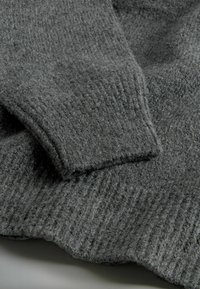 Grå strikket sweater med en tekstureret stof, ribbede manchetter og kanter, der giver et blødt og fuzzy udseende.