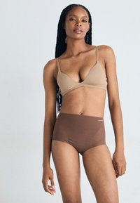Sutien bej căptușit cu bretele ajustabile, asortat cu chiloți maro cu talie înaltă. Ambele articole au o textură netedă și un design minimalist.
