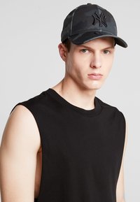 Black camo baseball cap featuring a curved bill, embroidered logo, and breathable fabric, worn with a sleeveless black shirt.