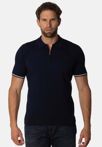 Polo de color navy con mangas cortas, que presenta un cuello con cremallera, una textura de canalé fina y acentos blancos en los dobladillos de las mangas.