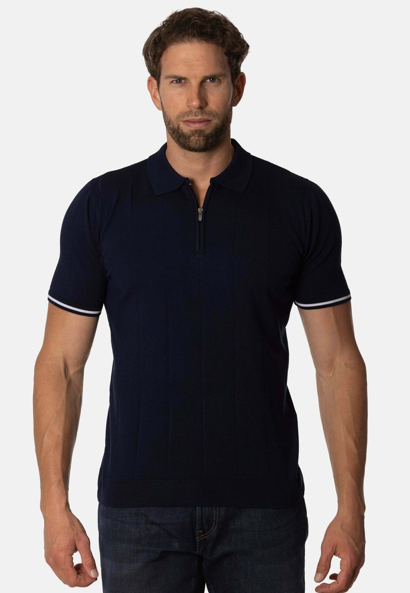 Polo de color navy con mangas cortas, que presenta un cuello con cremallera, una textura de canalé fina y acentos blancos en los dobladillos de las mangas.