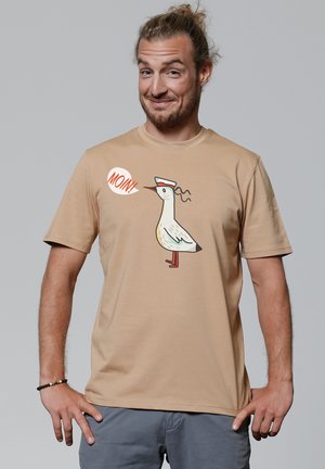 Beige T-Shirt mit kurzen Ärmeln, auf dem ein cartoonhaftes Vogel mit Hut und dem Wort "MOIN!" in einer Sprechblase abgebildet ist. Weicher Stoff und lockere Passform.