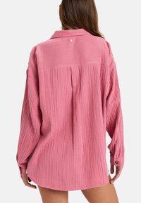 Rosa strukturierte Bluse mit langen Ärmeln, Kragen und einem Falten-Detail auf der Rückseite. Verfügt über eine Knopfschließe am Hals und am Bündchen. Lässige, übergroße Passform.