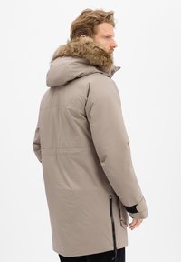 Heren beige parka jas met een met bont gevoerde capuchon, ritssluitingen aan de zijzakken en een licht taperende pasvorm bij de taille. Glad, waterdicht materiaal.