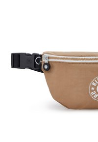 Tan nylon heuptas met een witte rits, zwarte verstelbare band en een cirkelvormig logodetail. Het heeft een gladde textuur en een compakte vorm.