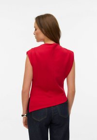 Top rojo sin mangas con cuello alto y aberturas laterales, hecho de una tela suave. La parte trasera presenta un detalle de costura central.