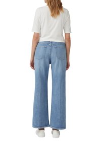 Jeans larges bleu clair en denim, avec une taille haute, deux poches arrière et un ourlet propre. Accompagné d'un haut blanc à manches courtes.