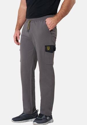 Man wearing gray cargo pants with elastic waist and drawstring, black patch on thigh pocket, and black sneakers. One hand in pocket.
