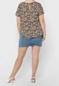 Blusa floreale a maniche corte con sfondo nero, caratterizzata da fiori colorati e un dettaglio a occhiello sulla schiena, abbinata a una gonna di jeans.