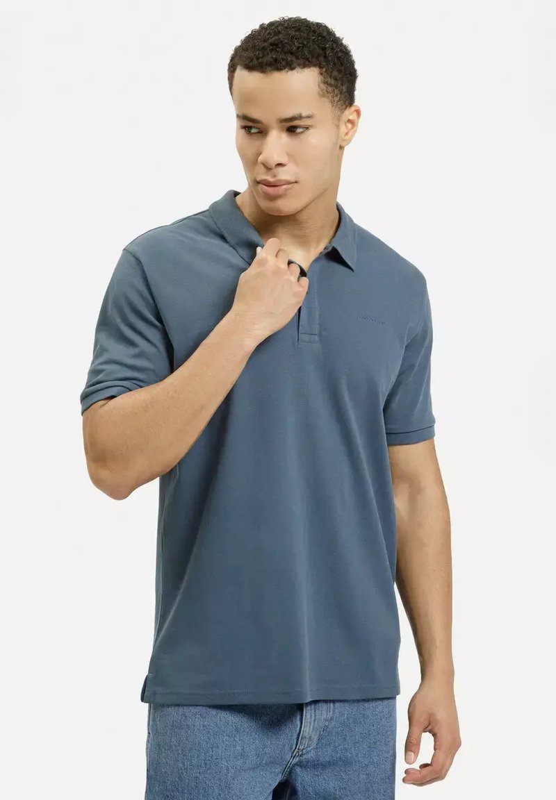 Niebieska bawełniana koszulka polo z kołnierzykiem, krótkimi rękawami i subtelną teksturą. Koszulka posiada małe logo na lewej piersi.