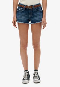 Shorts en denim bleu foncé avec des ourlets effilochés, associés à une ceinture tissée marron. Portés avec des baskets montantes noires.