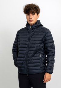 Giacca a vento navy con design trapuntato testurizzato, chiusura a zip completa e cappuccio attaccato. Caratterizzata da tasche laterali con zip e polsini elasticizzati.