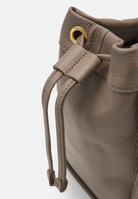 Bruine leren emmer tas met textuur, voorzien van een trekkoordsluiting en een goudkleurige veterring. Heeft gestikte randen en afgeronde hoeken.