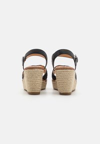 Sandalias de cuña negras con parte superior trenzada, correa alrededor del tobillo ajustable y tacón envuelto en yute. Plantilla de corcho con un acabado texturizado.