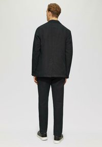 Herren schwarze Baumwolljacke mit geradem Schnitt, langen Ärmeln und sichtbaren Nähten, kombiniert mit passenden Hosen und lässigen schwarzen Schuhen.