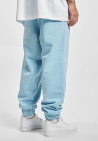 Pantaloni jogger de culoare albastru deschis, cu manșete elastice, confecționați dintr-un material moale, având o croială lejeră. Purtați cu adidași albi.