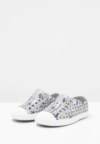 Zapatos grises de slip-on con agujeros abiertos, puntera de goma blanca y acentos azules, que cuentan con un diseño ligero y flexible, y una superficie texturizada.