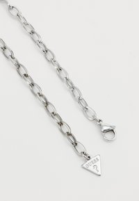 Silver chain link necklace featuring elongated oval links, a triangular "GUESS" charm, and a lobster clasp closure.