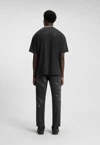 Sort kortærmet t-shirt med rund hals, parret med løstsiddende grå jeans med diagonale mønstre og sorte sko.
