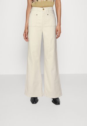 Korkeavyötäröiset, leveälahkeiset kermaiset housut, joissa on etutaskut, yhdistettynä mustiin kärjellisiin kenkiin ja kuviolliseen neulepaitaan.