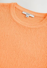 Maglione lavorato a maglia di un arancione chiaro con una finitura testurizzata. Presenta un collo a giro e un'etichetta con la scritta "NEXT" cucita all'interno.
