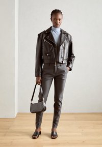 Zwart leren cropped jack met zilveren hardware, gecombineerd met slanke grijze broeken en een kleine zwarte gestructureerde handtas. Zwarte slide sandalen maken de look compleet.