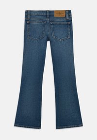 Jean en denim bleu foncé évasé avec une texture lisse, deux poches arrière et une étiquette en cuir marron au niveau de la taille.