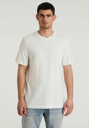 T-shirt bianco a maniche corte realizzato in cotone, con scollo rotondo e un piccolo logo sul lato sinistro del petto. Abbinato a jeans chiari strappati.