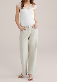 Vit ribbad tanktop med spetsärmar, kombinerad med ljusbeiga vida byxor. Slät textur, framfickor och minimal detaljering.