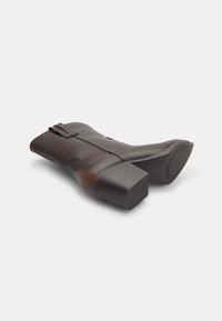 Botine maro din piele, cu toc pătrat, cusături pe lateral și o curea decorativă pe partea superioară. Textură netedă și design minimalist.