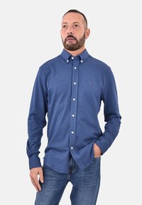 Camicia a maniche lunghe blu da uomo in tessuto misto cotone, con colletto, bottoni bianchi e un piccolo logo sul petto.