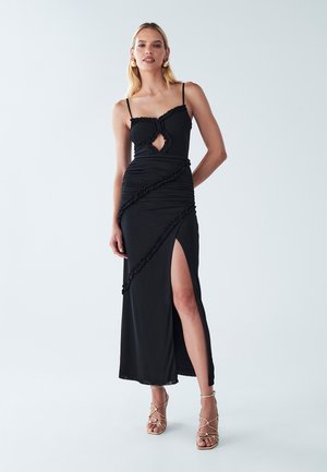 Black maxi dress with spaghetti straps, keyhole cutout, and ruffled detailing. Features a side slit and ruched texture. Paired with gold strappy sandals.