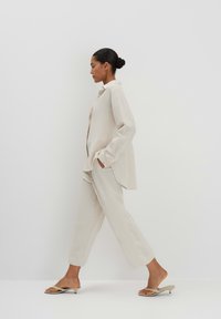 Lichtbeige outfit met een losvallend shirt met lange mouwen en een slimfit broek, gecombineerd met minimalistische, platte instappers.