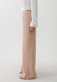 Vidbygd byxor i ljusrosa tyg, med en glatt textur och skräddarsydd design. Minimalistiska med rena linjer och utan synliga utsmyckningar.