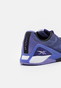 Talons de sneaker Reebok Nano X1 en violet et noir avec une semelle blanche et un tissu en maille, affichant les logos de la marque et le texte "Floatride Energy".