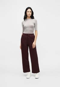 Haut gris côtelé à manches courtes associé à un pantalon de survêtement bordeaux ample avec taille élastique et cordon de serrage. Le mannequin porte des baskets blanches.