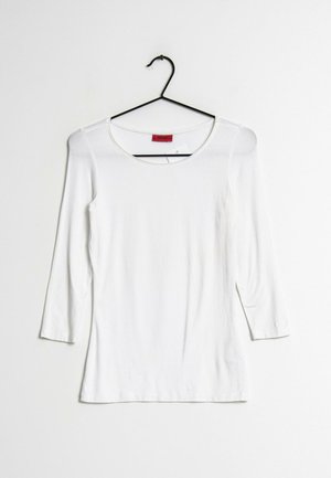 Chemise blanche à manches longues avec encolure ronde sur un cintre noir, sur fond blanc uni.