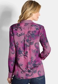 Langachtige zijden blouse in levendig paars met blauw paisley- en bloempatronen, voorzien van een knoopsluiting aan de achterkant en een enkele borstzak.