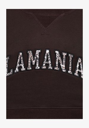 Csillogó flitteres betűk alkotják az "ALLAMANIAN" szót egy ívben, sötétbarna anyagon, látható varrással a nyakkivágásnál és az aljánél.