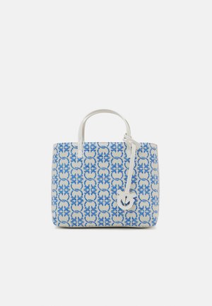 Bolso tote blanco y azul con patrón geométrico, asas dobles y una etiqueta de cuero con un diseño recortado colgando de una de las asas.