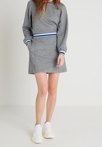 Sudadera gris con acentos azul rayados, combinada con una mini falda gris a juego. Ambas prendas están hechas de una tela suave y lisa. Zapatillas blancas completan el look.