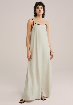 Vestido maxi verde claro con tirantes negros finos y un acabado texturizado. Corte suelto que cae hasta el suelo, combinado con sandalias negras.