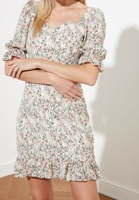 Robe courte à fleurs avec des manches bouffantes, un décolleté carré et un ourlet à volants ; disponible en blanc, vert et rose avec un motif délicat.