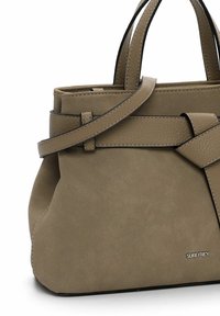 Warme taupe Handtasche aus strukturiertem Leder, mit flachem Tragegurt, genähten Akzenten und einem dezenten Logo an der Unterseite. Strukturierte Form.